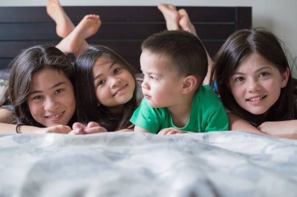 Siblings lying on a bed together stock photo