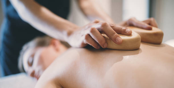 istock Massage therapist using wooden tool to massage patient 980749544