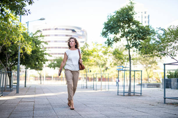 Mature businesswoman walking on footpath in city Full length of mature businesswoman walking on footpath. Female professional is looking away in city. She is wearing smart casuals. older woman purse stock pictures, royalty-free photos & images