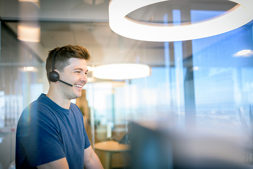 Smiling businessman using wireless headphones in office. Confident mid adult customer service representative is looking away. Professional is wearing smart casual in call centre.
