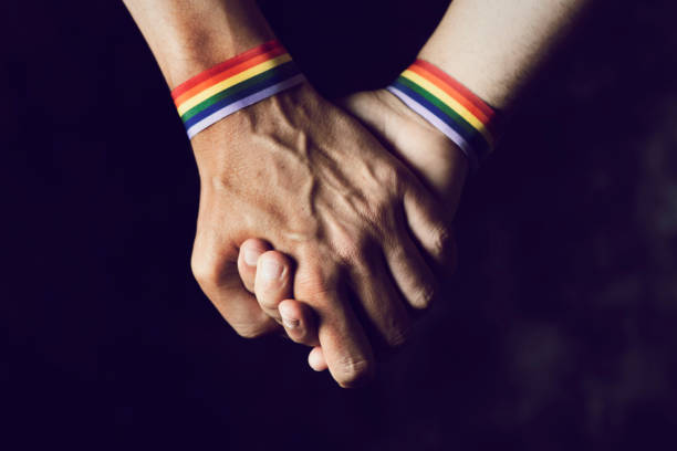 men holding hands with rainbow-patterned wristband closeup of two caucasian men holding hands with a rainbow-patterned wristban on their wrists marriage equality stock pictures, royalty-free photos & images