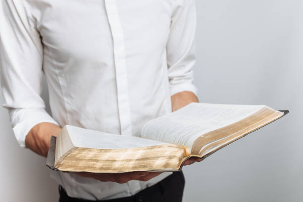 istock Man reading Bible, white background, book in hand close-up 980772454