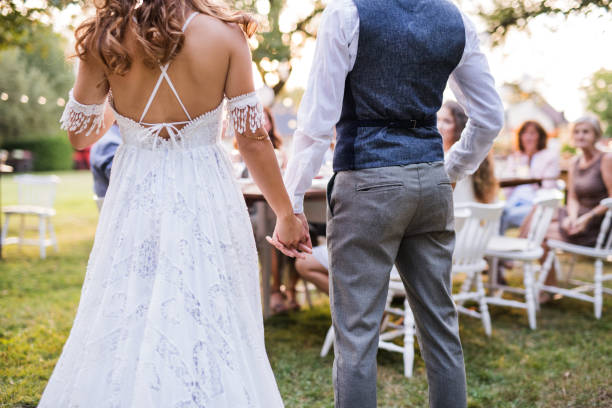 istock Unrecognizable bride and groom with guests at wedding reception outside in the backyard. 980790312