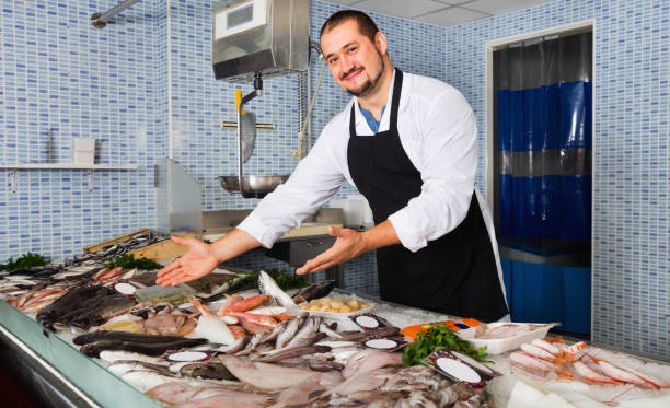 istock Seller in black apron showing fish on his counter 980803080