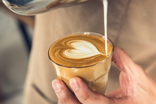 Professional barista holding coffee cup making beautiful heart shape latte art