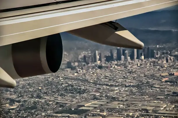 Partial view of airplane wing in flight with Los Angeles city in the background, as plane approaches LAX; focus on wing.
