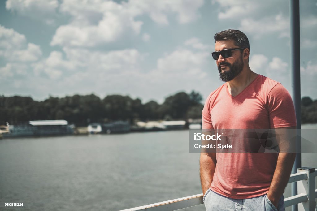 Bearded macho man standing by the river Bearded macho man standing by the river with hands in his pockets Men Stock Photo