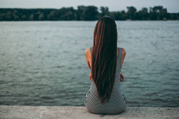 istock Attractive girl sitting alone by the water 980818260
