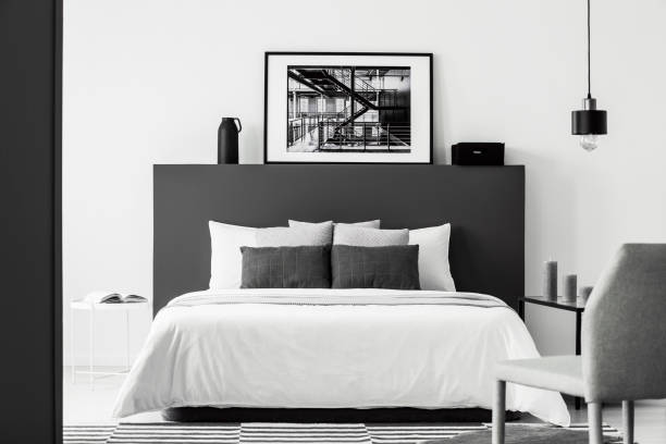 Poster in contrast bedroom interior Poster on black bedhead of white bed in contrast bedroom interior with grey chair and lamp monochrome house stock pictures, royalty-free photos & images