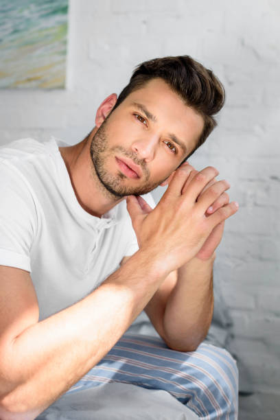 istock handsome young man in pajamas sitting on bed and looking at camera 980848392