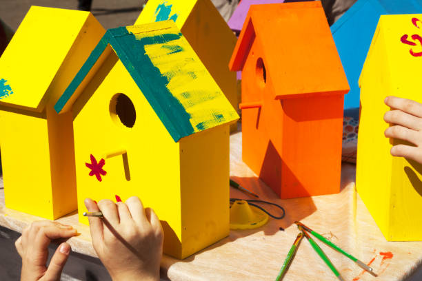 Children painting birdhouses bright colors of orange and yellow Kids woodcraft lesson, making wooden houses for birds nesting box stock pictures, royalty-free photos & images