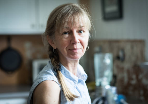 60-letnia urocza drobna kobieta z naturalnym światłem w kuchni - braided women sensuality portrait zdjęcia i obrazy z banku zdjęć