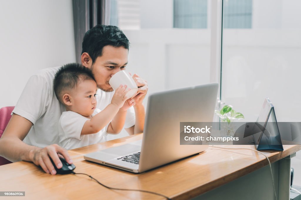 Asian little son helping father drinking coffee between working with laptop computer notebook at workplace happy family together at home concept. Father Stock Photo