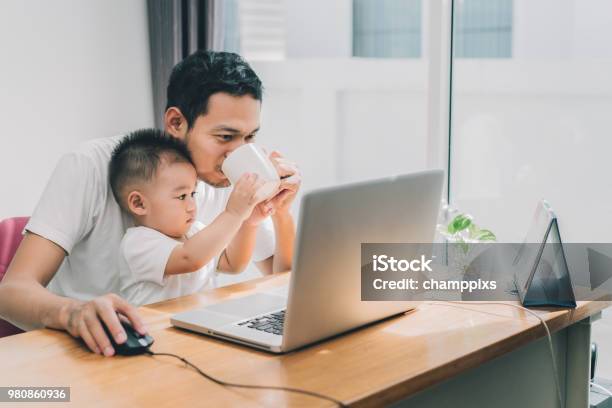 Asian Little Son Helping Father Drinking Coffee Between Working With Laptop Computer Notebook At Workplace Happy Family Together At Home Concept Stock Photo - Download Image Now