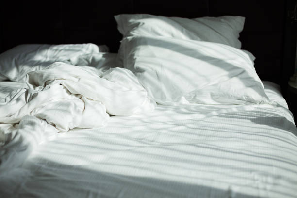 istock Messy bedding sheets and pillows, sunshine through window in the morning 980862952