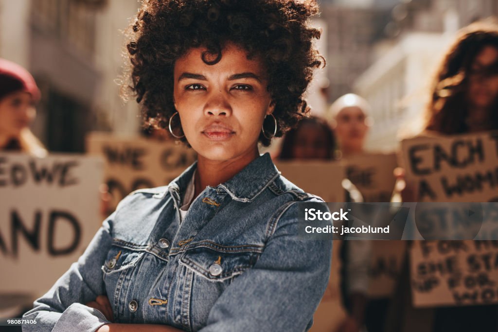 Woman protesting with group of activists Young black woman with group of demonstrator in background outdoors. African woman protesting with group of activists outdoors on road. Protest Stock Photo