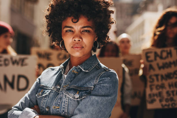 Woman protesting with group of activists Young black woman with group of demonstrator in background outdoors. African woman protesting with group of activists outdoors on road. womens rights photos stock pictures, royalty-free photos & images