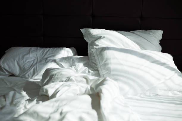 istock Messy bedding sheets and pillows, sunshine through window in the morning 980875182
