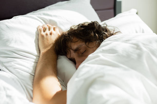 istock Blond men is sleeping alone in bed with white bedclothes (selective focus) 980875302