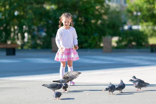 Beautiful girl gives bread to the birds on the city street.