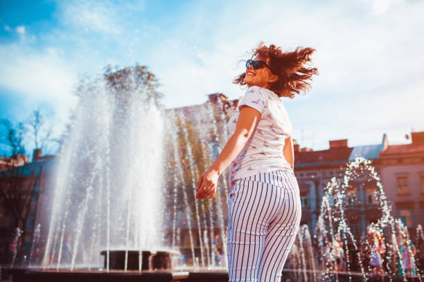 счастливая молодая женщина работает и танцует у фонтана на летн�ей улице - dancing fountains стоковые фото и изображения