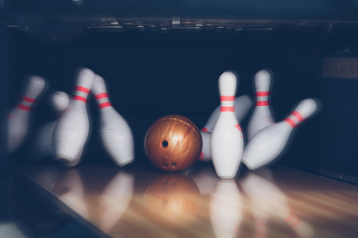 Red bowling ball hitting pins in the bowling alley on white background. Horizontal composition with copy space. Bowling concept.