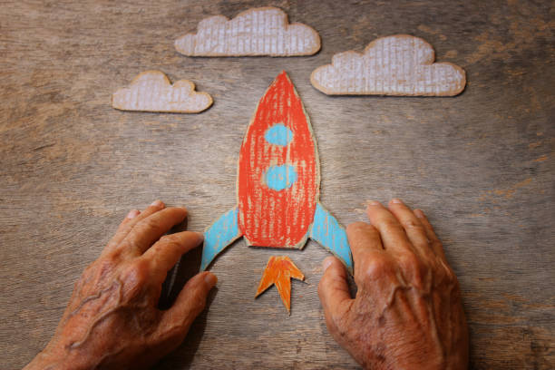 a close-up de um homem idoso segurando um foguete de papel em uma mesa de madeira. conceito de pensar sobre os sonhos de infância, a tristeza e a solidão - distress rocket - fotografias e filmes do acervo