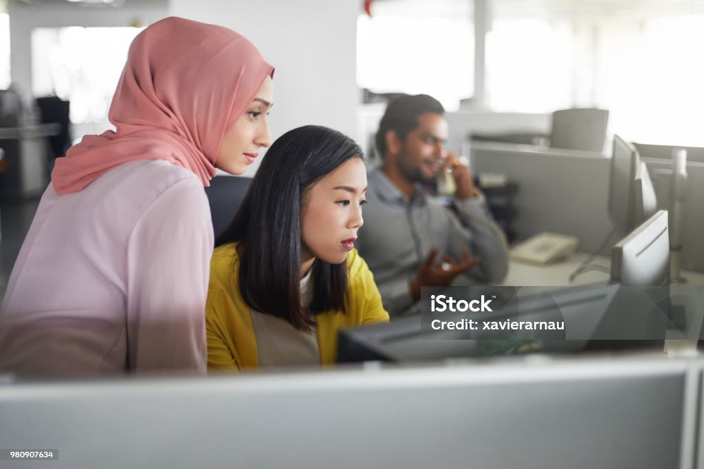 Female colleagues working at computer desk Businesswomen discussing over desktop PC in office. Female colleagues are looking in computer monitor. They are at workplace. Multiracial Group Stock Photo