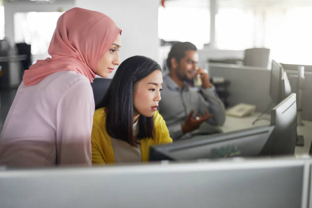 Female colleagues working at computer desk Businesswomen discussing over desktop PC in office. Female colleagues are looking in computer monitor. They are at workplace. east asian ethnicity stock pictures, royalty-free photos & images