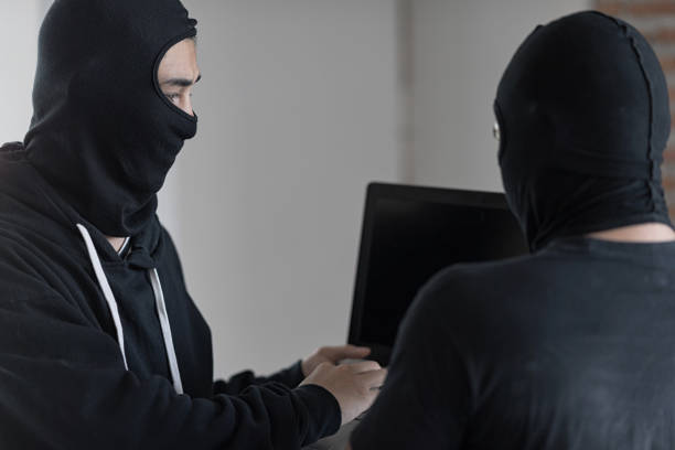 istock Two black masked hackers are using laptop. They are trying to hack data. Selective focus at hacker' face. 980926704