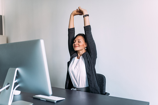 Break at work. Female office worker stretching hands.
