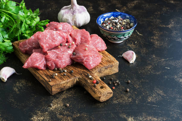 istock Raw meat of beef slices with spices on a dark background. selective focus, copy space. 980960266