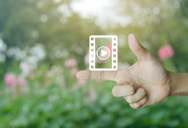 Play button with movie icon on finger over blur pink flower and tree, Cinema online concept