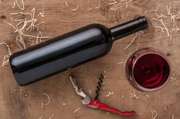 Wine bottle, glass of red wine and corckscrew flatlay composition over a wooden rustic table.