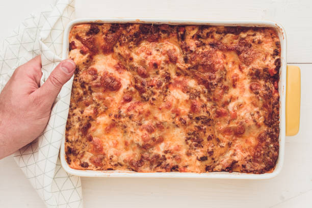 istock Hand Serves Italian Lasagna Bolognese with Beef, Tomato Sauce and Green Basil on Rustic White Wooden Table 980973254