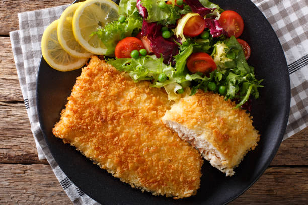 istock Fried fish fillet in breading and fresh vegetable salad close-up. horizontal top view 980989656
