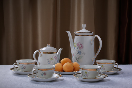 White traditional porcelain tea set with flowers and plate with apricots on a white tablecloth