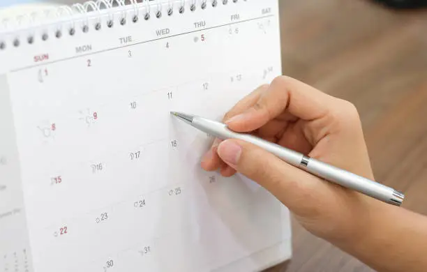 close up on woman hand with pen writing on calender for note or make appointment concept.