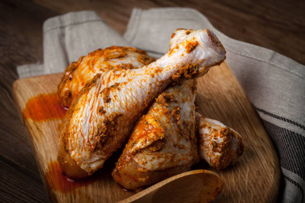 istock Marinated chicken drumsticks on a wooden chopping board. 981054526
