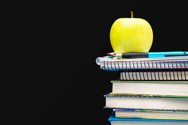 istock Green apple on stack of school supplies against black background. Space for text. 981064792