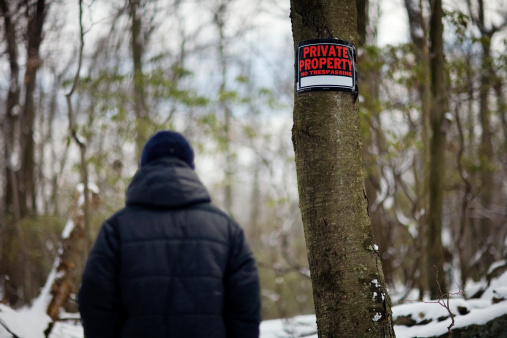 Man walking past a Private Property sign in the snowy woods.