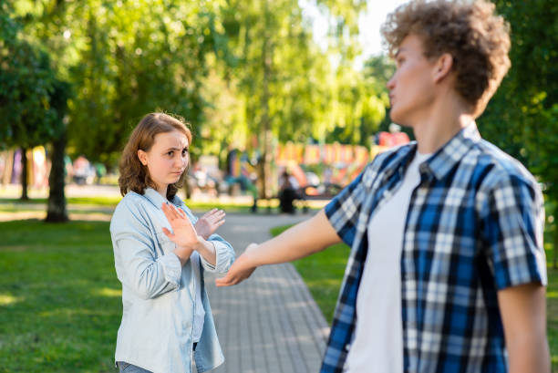 young man in summer in a park outdoors. tries to get acquainted with a beautiful girl. the girl gestures to show no. unwillingness to talk. the concept of dating in the city. - unwillingness imagens e fotografias de stock