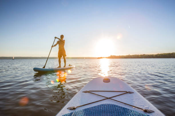 volle länge des mannes auf dem paddelbrett im meer während des sonnenuntergangs - ammersee stock-fotos und bilder