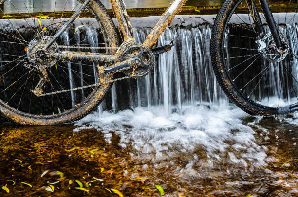A dirty mountain bike stands in a creek against the waterfall. Dirty chain drive Mountain bike close-up