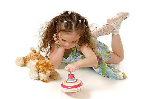 Little beautiful girl sitting on carpet, looking at camera and playing with a smile.