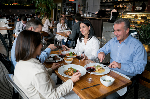 Happy group of adult people eating together at a restaurant and smiling