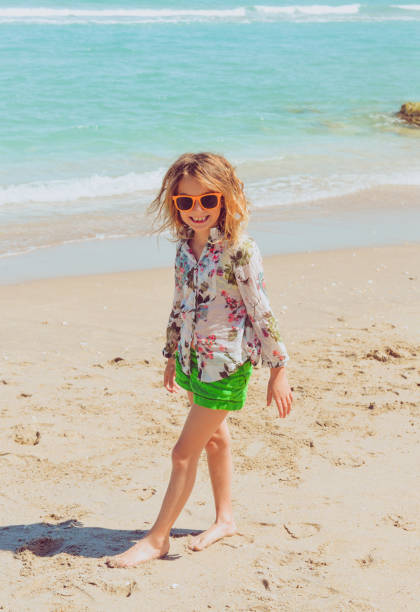 Little Tourist in Paradise Adorable 7 year old girl in sunglasses on a stunning idyllic beach near the ocean in a tropical paradise. Full of smiles and joy and sunny island vibes hawaiian shirts for kids stock pictures, royalty-free photos & images