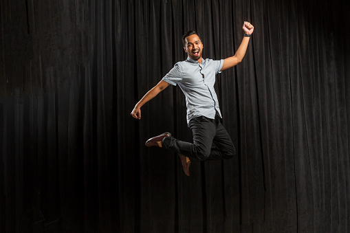 Studio portrait on a black background of a happy young Asian man jumping in the air