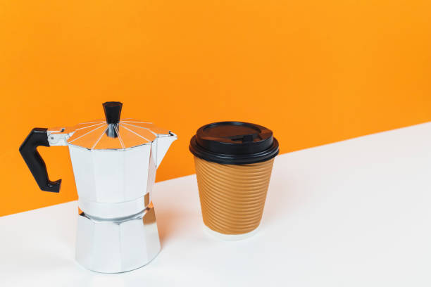 istock Coffee espresso maker with a paper coffee cup on a white table and orange wall background.Template mock up for adding your design. 981331976