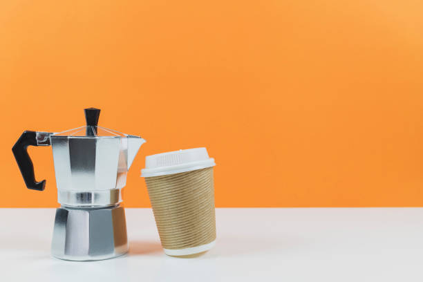 istock Coffee espresso maker with a paper coffee cup on a white table and orange wall background.Template mock up for adding your design. 981331984